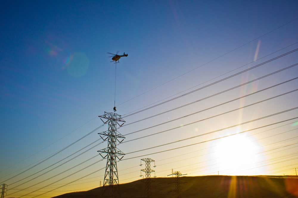 man hanging below helicopter working on lines